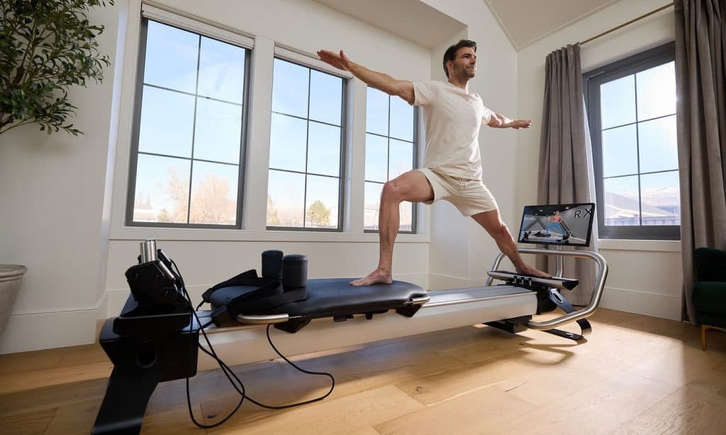 Individual performing a controlled reformer exercise on a Pilates reformer in a bright home setting, demonstrating guided strength and alignment work.