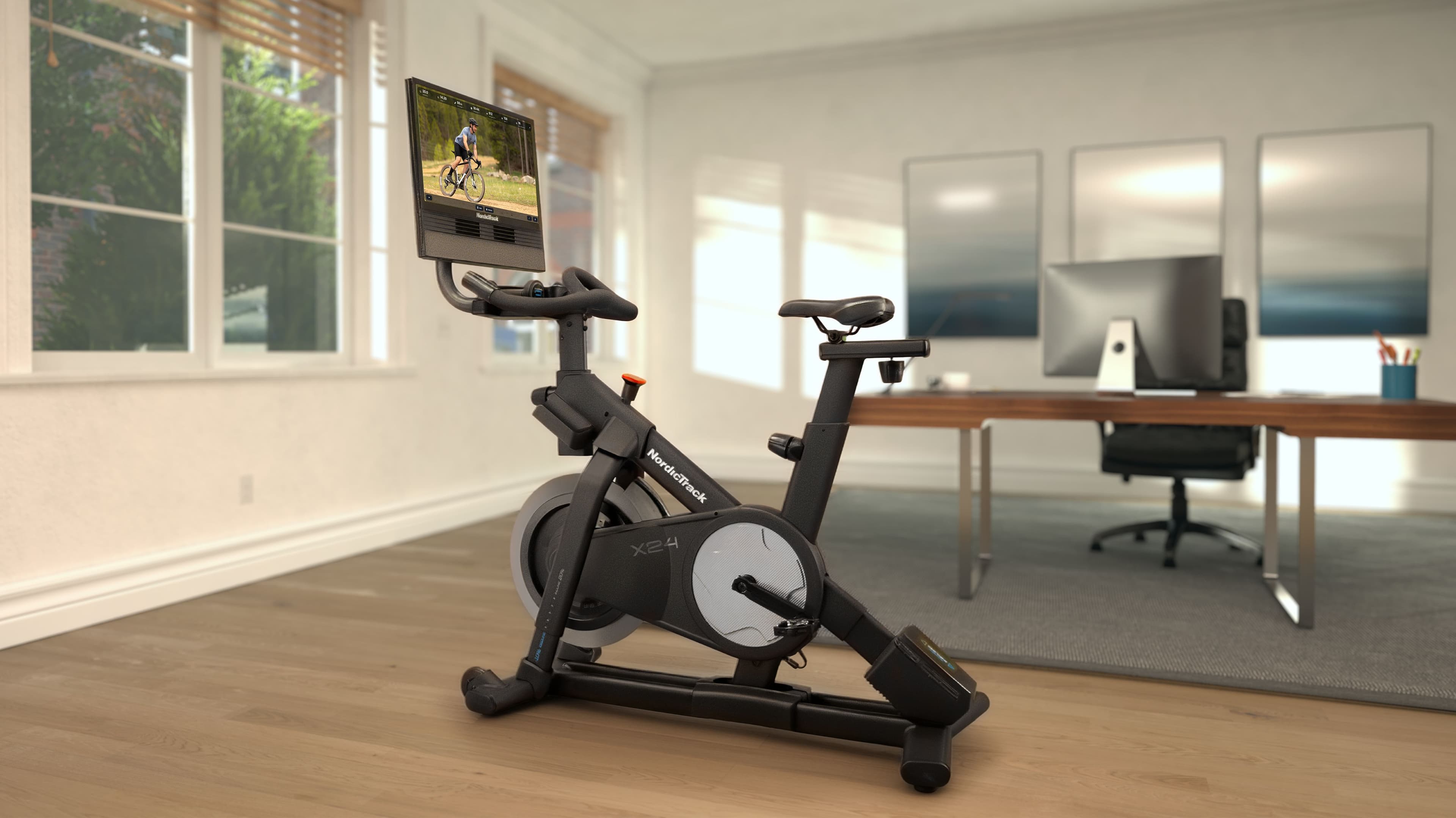 NordicTrack X24 Bike with 24-inch HD touchscreen streaming an outdoor cycling workout in a home office setting