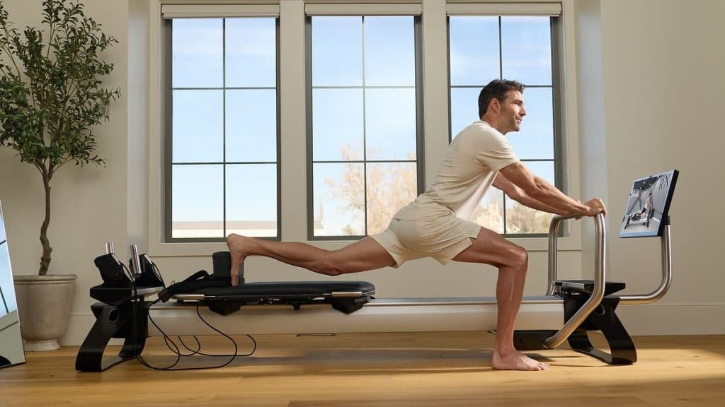 A practitioner performs a dynamic lunge on the Ultra 1 Reform RX-S, showcasing performance-driven reformer Pilates in a bright, structured studio space.