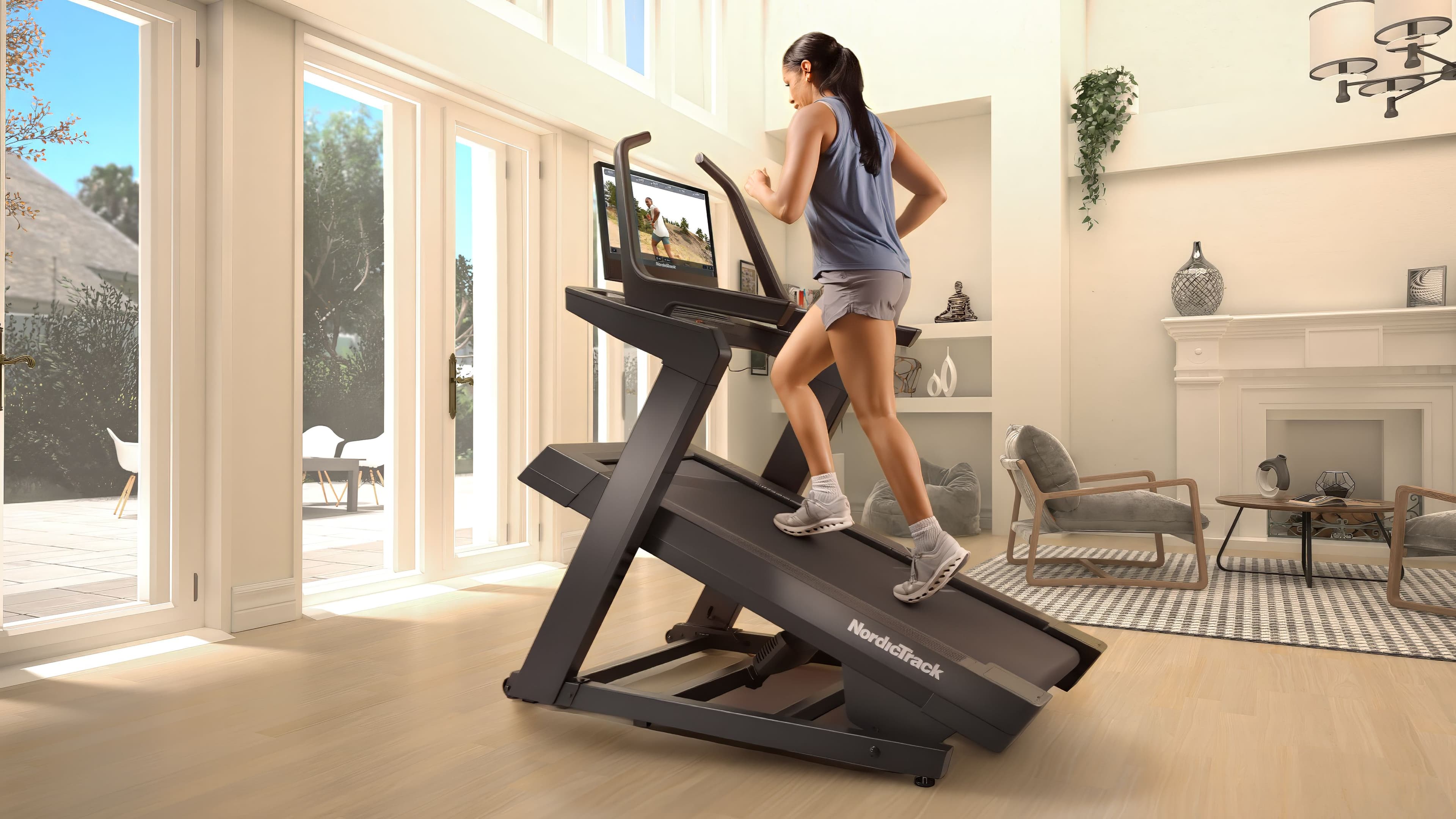 Woman walking at high incline on a NordicTrack X24 treadmill in a bright home living room with large windows
