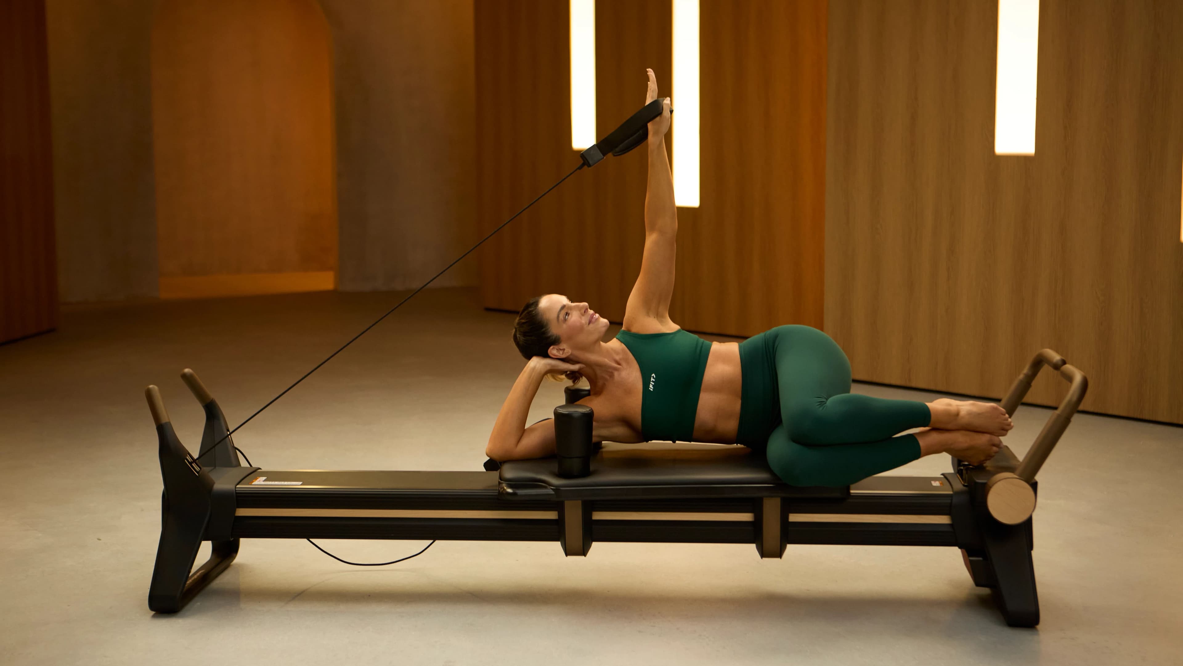 A Pilates instructor demonstrating a side-lying leg series on a reformer machine, highlighting the use of the carriage and straps for controlled, supported resistance.