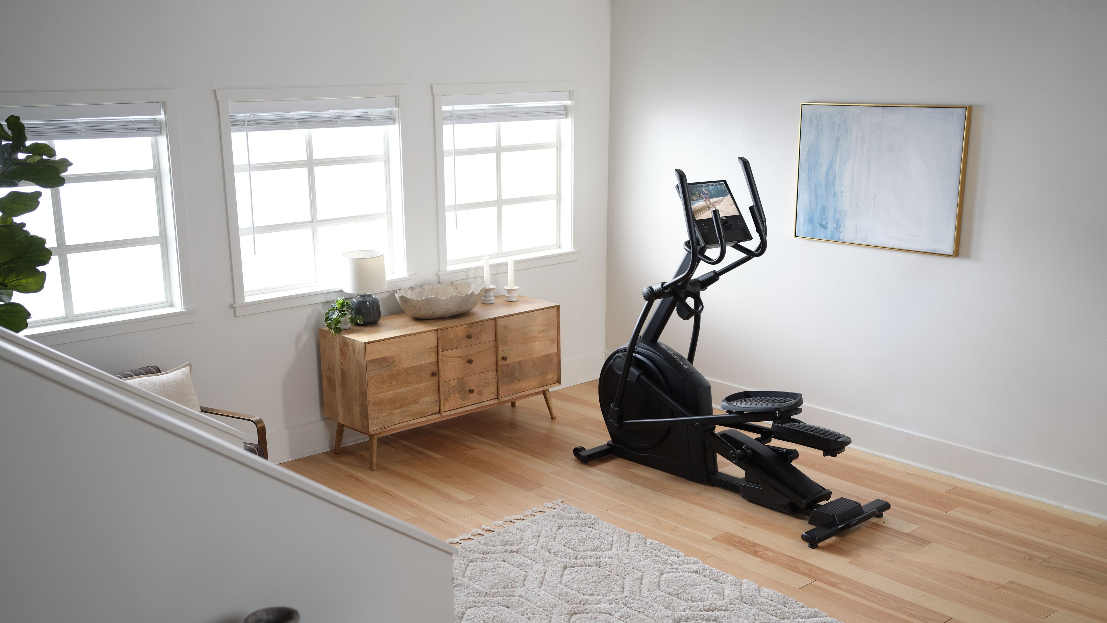 NordicTrack AirGlide 16 elliptical in a minimalist white home room with hardwood floors, iFIT touchscreen visible