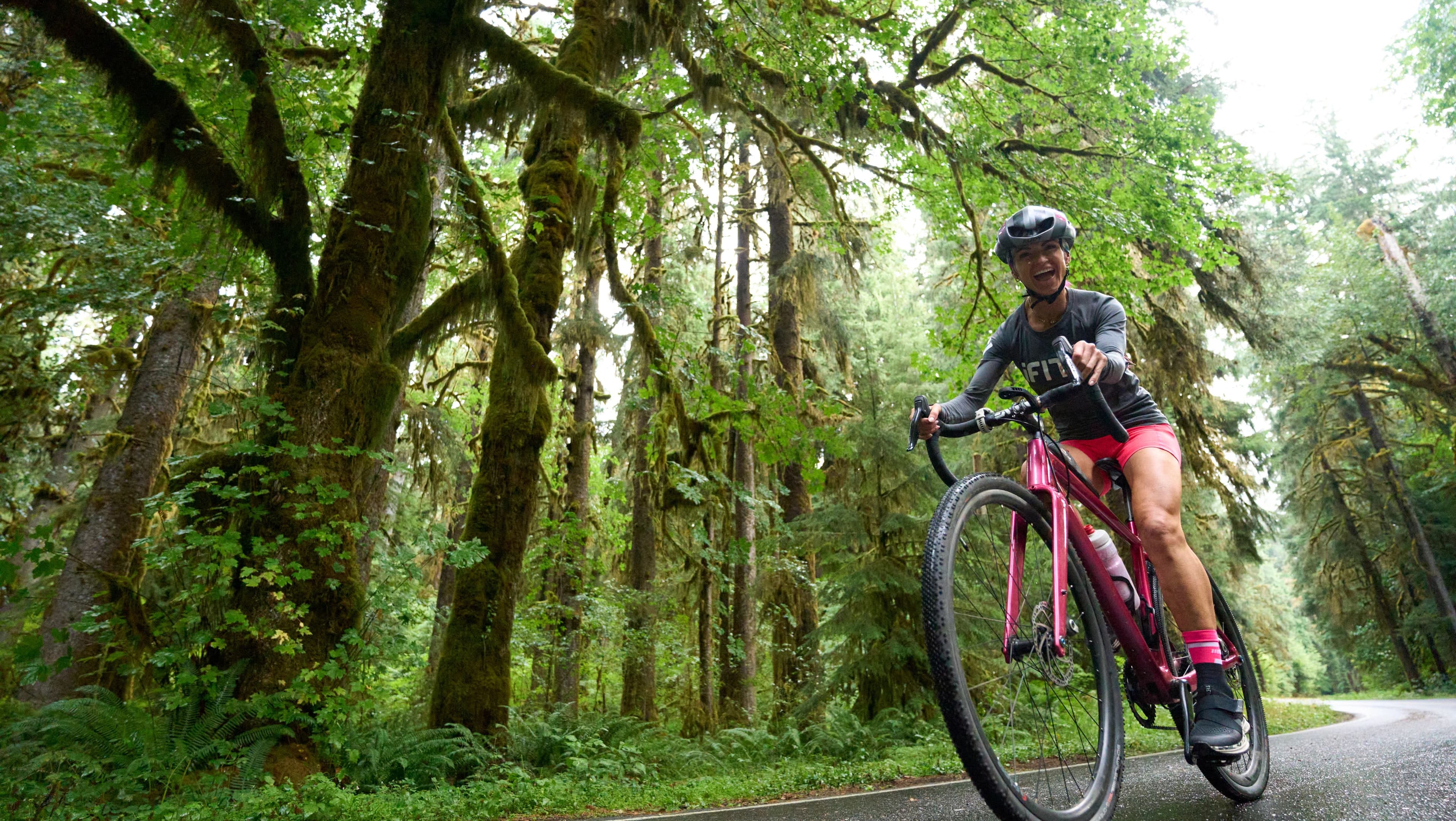 iFIT trainer Ashley Paulson riding through a moss-covered old-growth rainforest road on the Washington National Parks Power and Incline Cycling Series