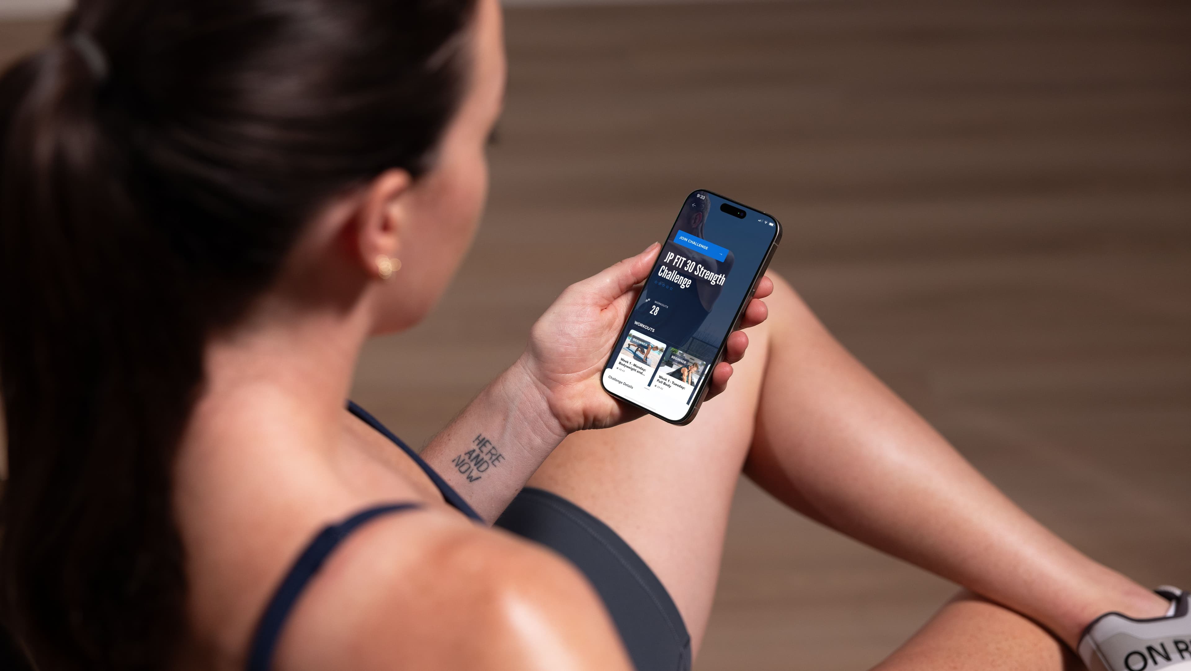 Close-up of a woman holding a phone displaying an iFIT strength challenge in the iFIT app