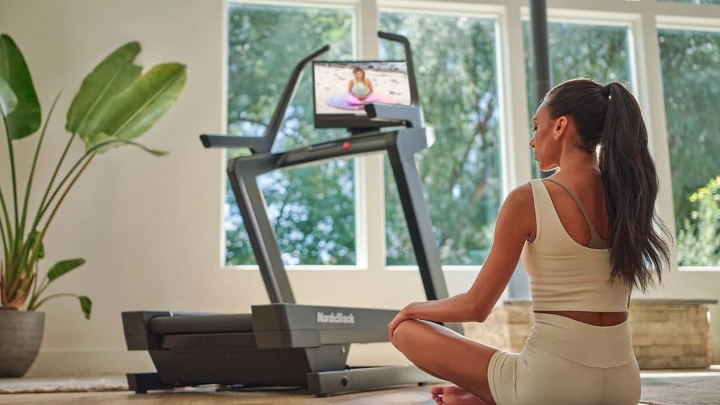 A user follows a guided iFIT workout on a NordicTrack treadmill in a bright home setting, illustrating immersive at-home cardio training.